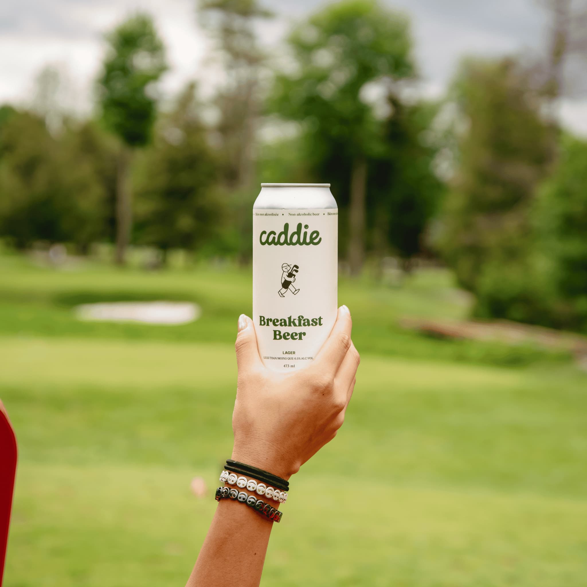 Caddie Breakfast Beer held by hand with golf course in background